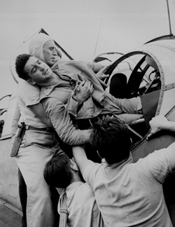 Crewmen lifting Kenneth Bratton out of turret of TBF on the USS SARATOGA after raid on Rabaul." Lt. Wayne Miller, November 1943. 80-G-415477