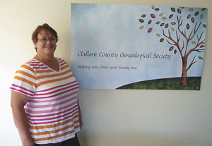 Virginia Majewski, president of the Clallam County Genealogical Society, poses with the group’s logo in its new research center. Sequim Gazette photo by Patricia Morrison Coate.